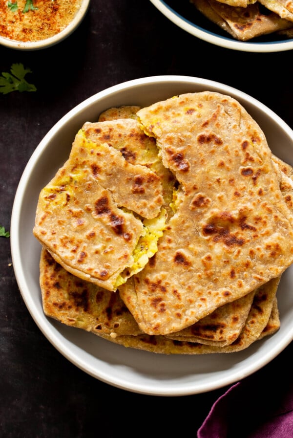 aloo paratha pilled up on a plate, top one is torn open, so you can see the filling