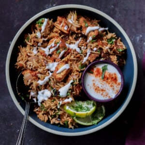 Lucknowi biryani in a bowl topped with raita and a ramekin of raita on the side