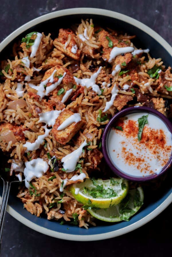 Lucknowi biryani in a bowl topped with raita and a ramekin of raita on the side