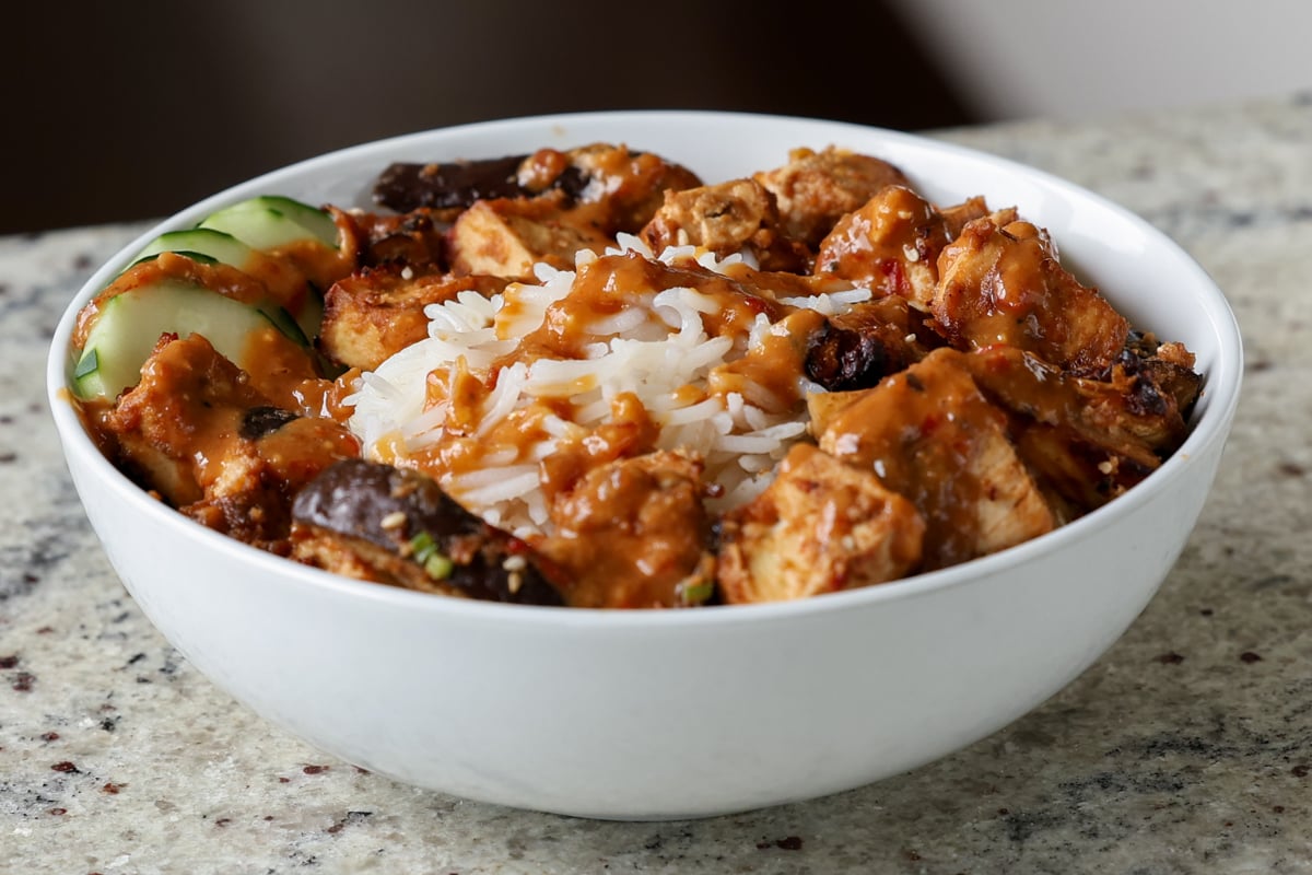 eggplant and tofu in the bowl with rice with sauce drizzled on top