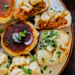 serving plate of butter chicken bao with one flipped so you can see the crispy bottom and one town in half so you can see the filling