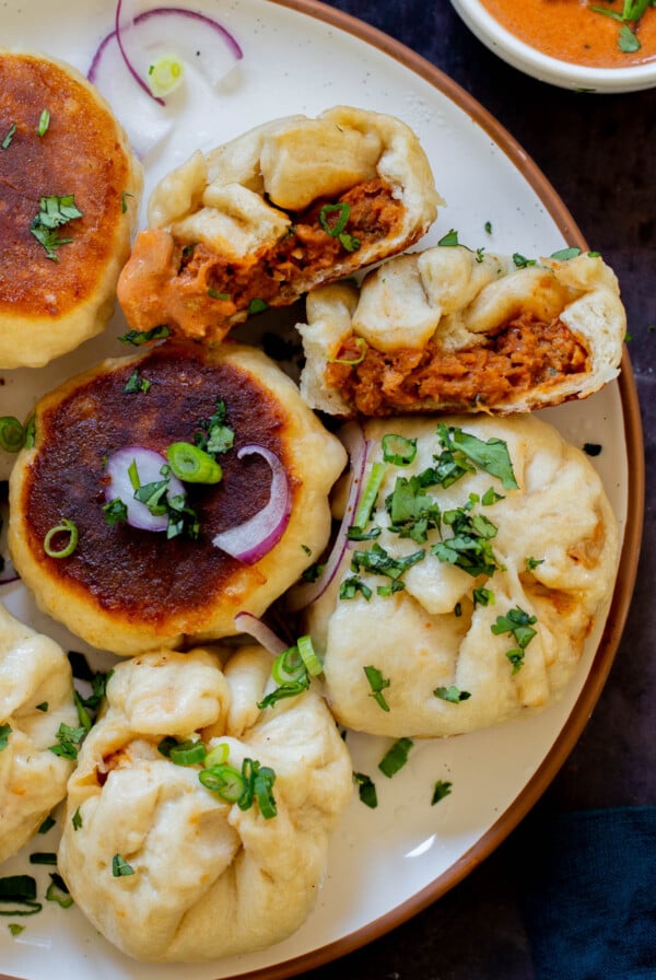 serving plate of butter chicken bao with one flipped so you can see the crispy bottom and one town in half so you can see the filling