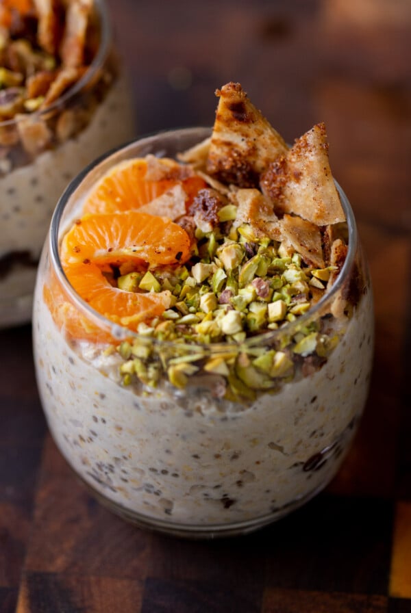 cannoli overnight oats in a glass topped with oranges, pistachios, and crispy cinnamon sugar tortilla pieces