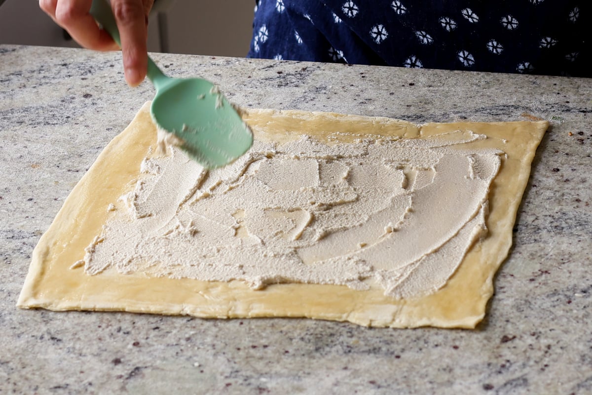 spreading cream cheese onto rolled out puff pastry