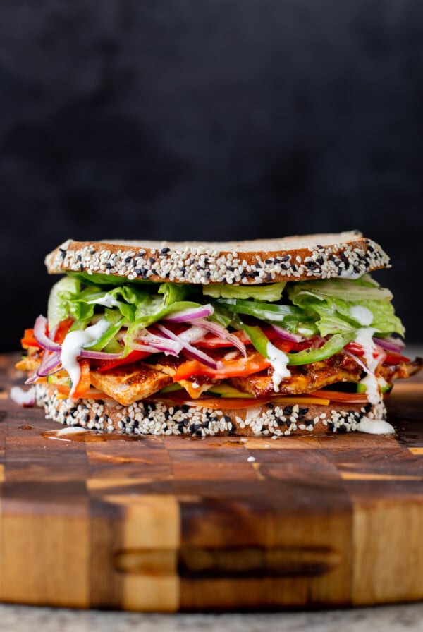 vegan club sandwich with veggies and tofu deli meat on a wooden cutting board