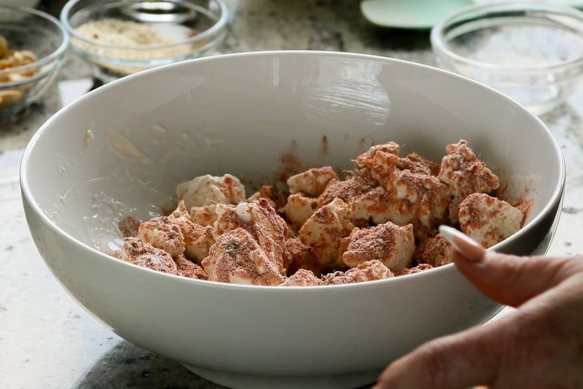 tossing tofu with spices and yogurt in a bowl