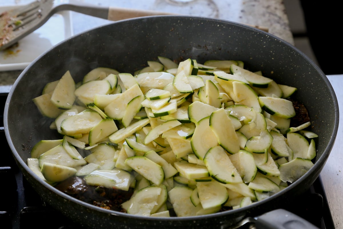 adding zucchini to the pan of spices