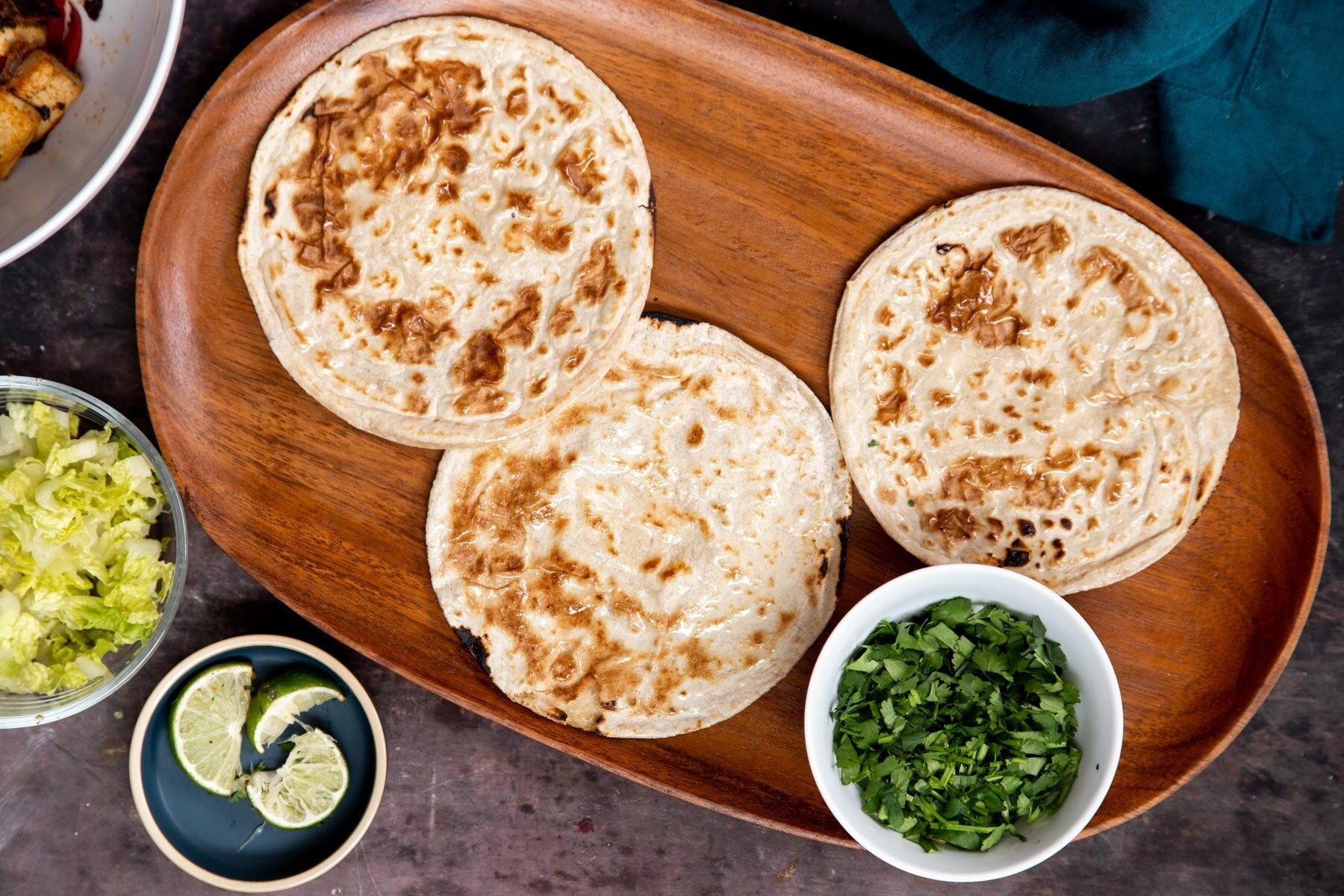 three small tortillas on a wooden platter surrounded by bowls with taco toppings 