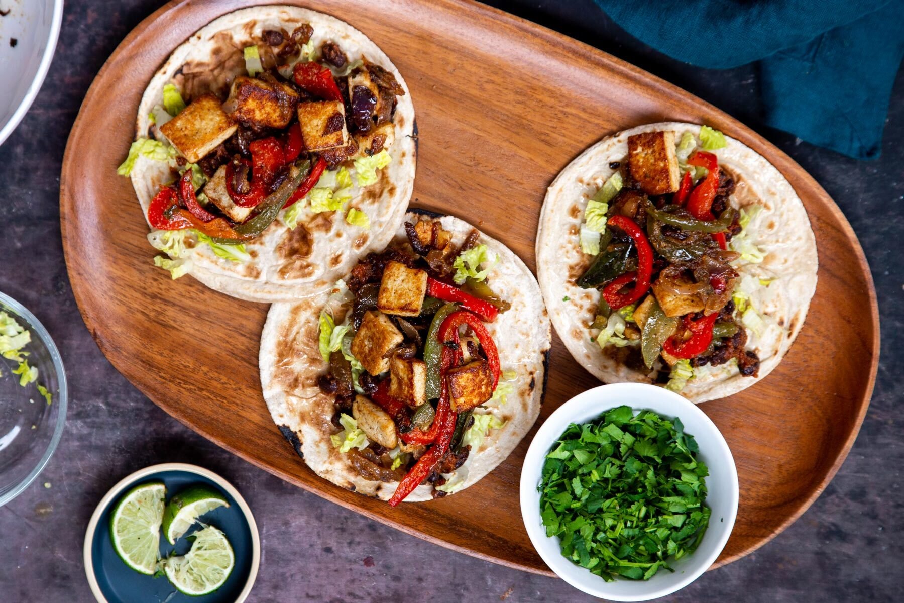 three tacos with lettuce, bell peppers, black beans and fried smoky tofu on a wooden platter