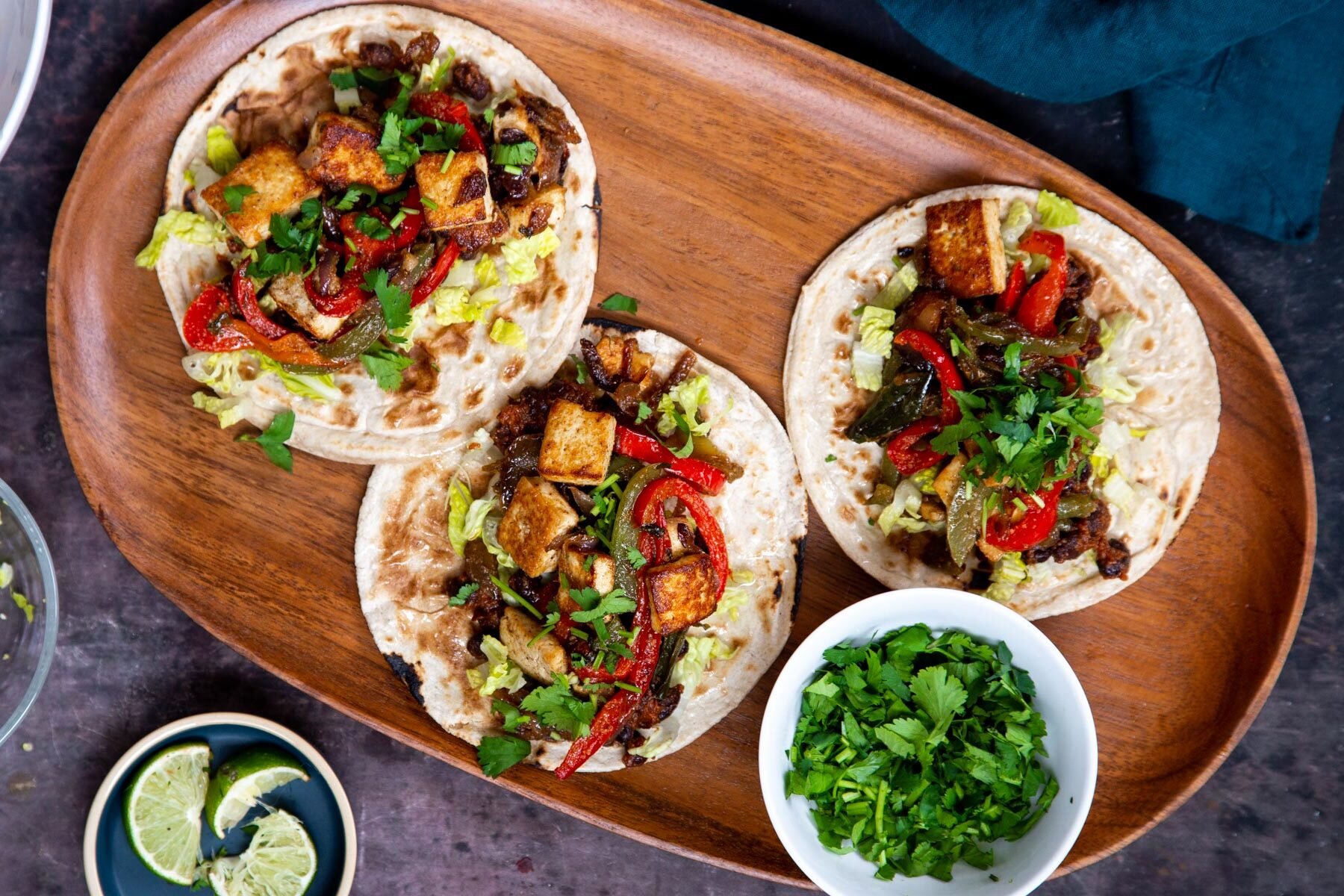 small wheat tortillas on a wooden platter topped with tofu, bell peppers and black beans 