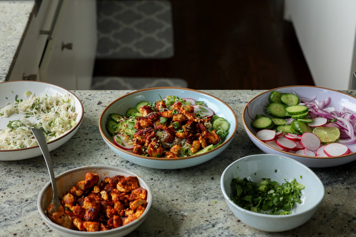 harissa tofu bowl surrounded by all of the prepped ingredients