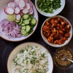 harissa tofu, herbed rice, fresh veggies, herbs, and dressing in bowls on a dark table