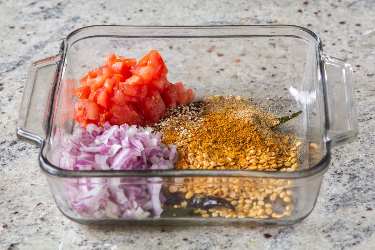 onions, lentils, tomatoes, and tempering in a glass casserole dish