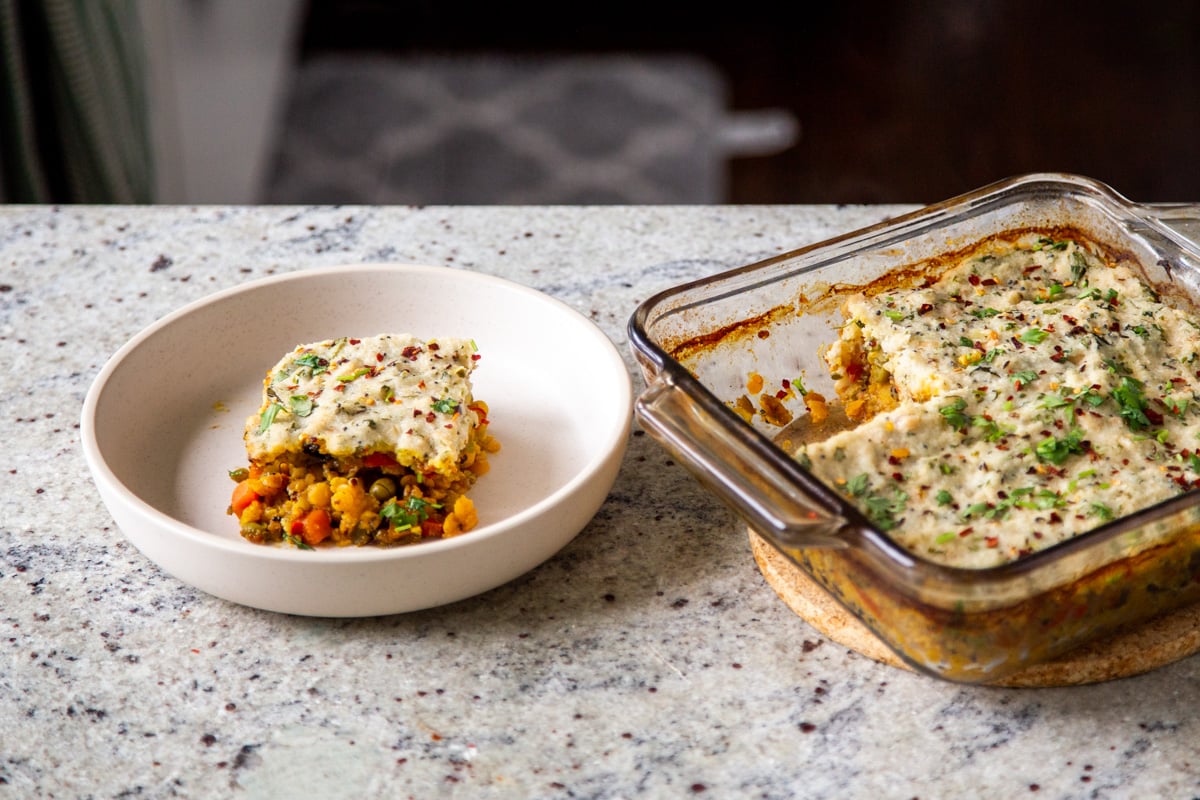 freshly baked idli sambhar casserole on a kitchen counter with a plate with once square cut 