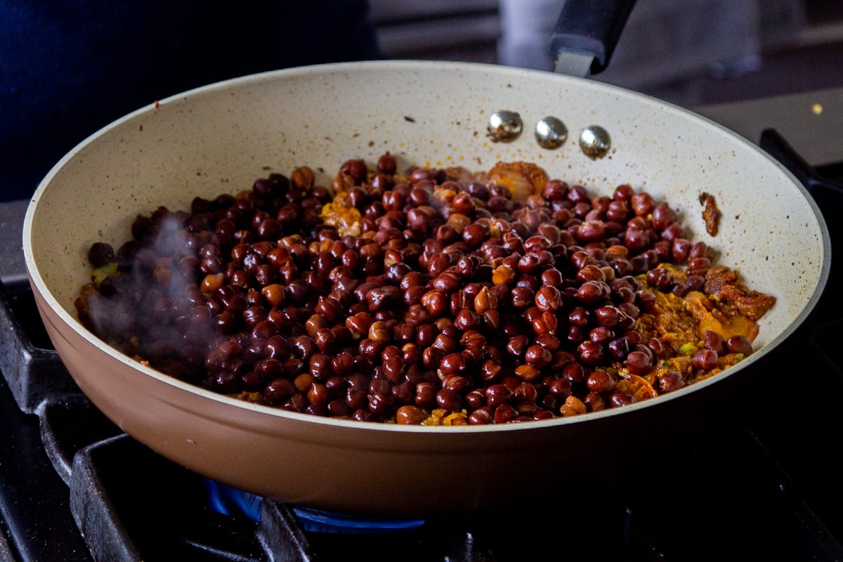 adding the cooked brown chickpeas to the pan