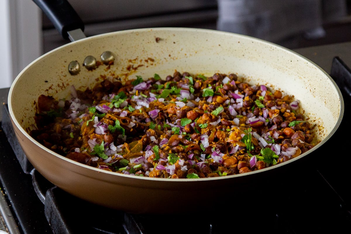 ghugni garnished with onions and cilantro in the frying pan