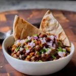 ghugni garnished with onions, cilantro, and cumin in a bowl with flatbread