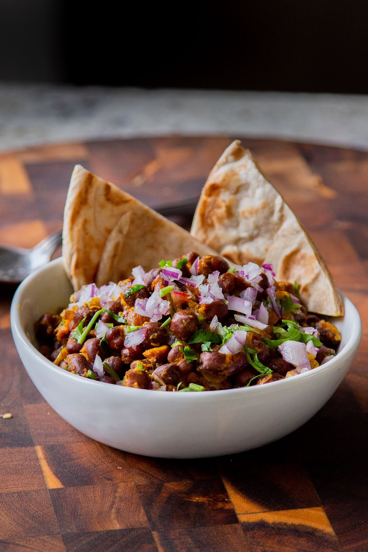 ghugni garnished with onions, cilantro, and cumin in a bowl with flatbread