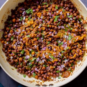 ghugni garnished with onions, cilantro, and cumin in the frying pan