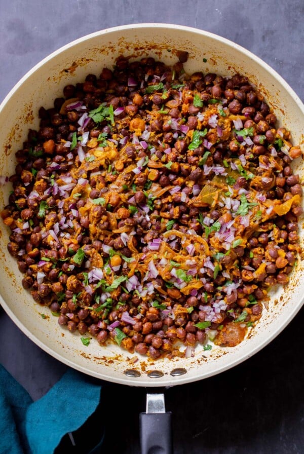 ghugni garnished with onions, cilantro, and cumin in the frying pan