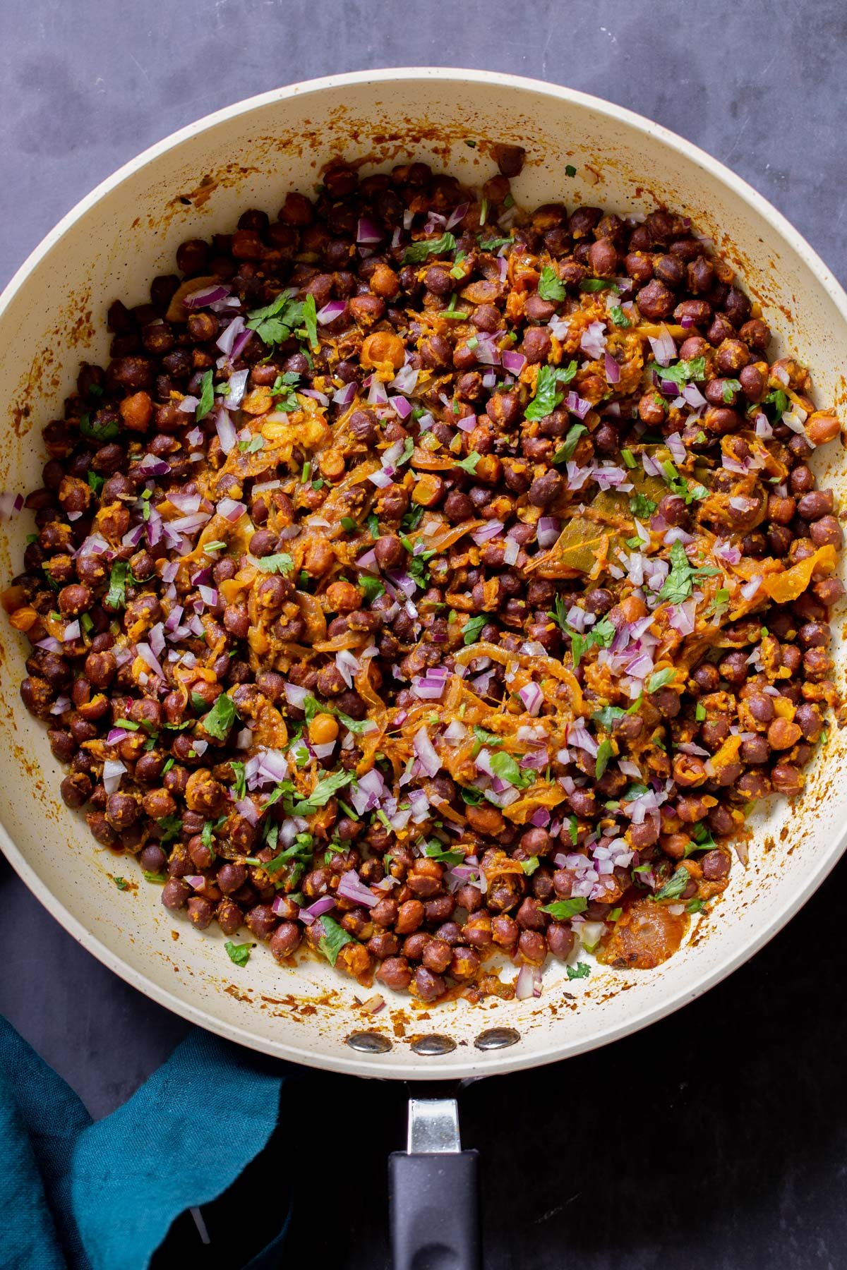 ghugni garnished with onions, cilantro, and cumin in the frying pan