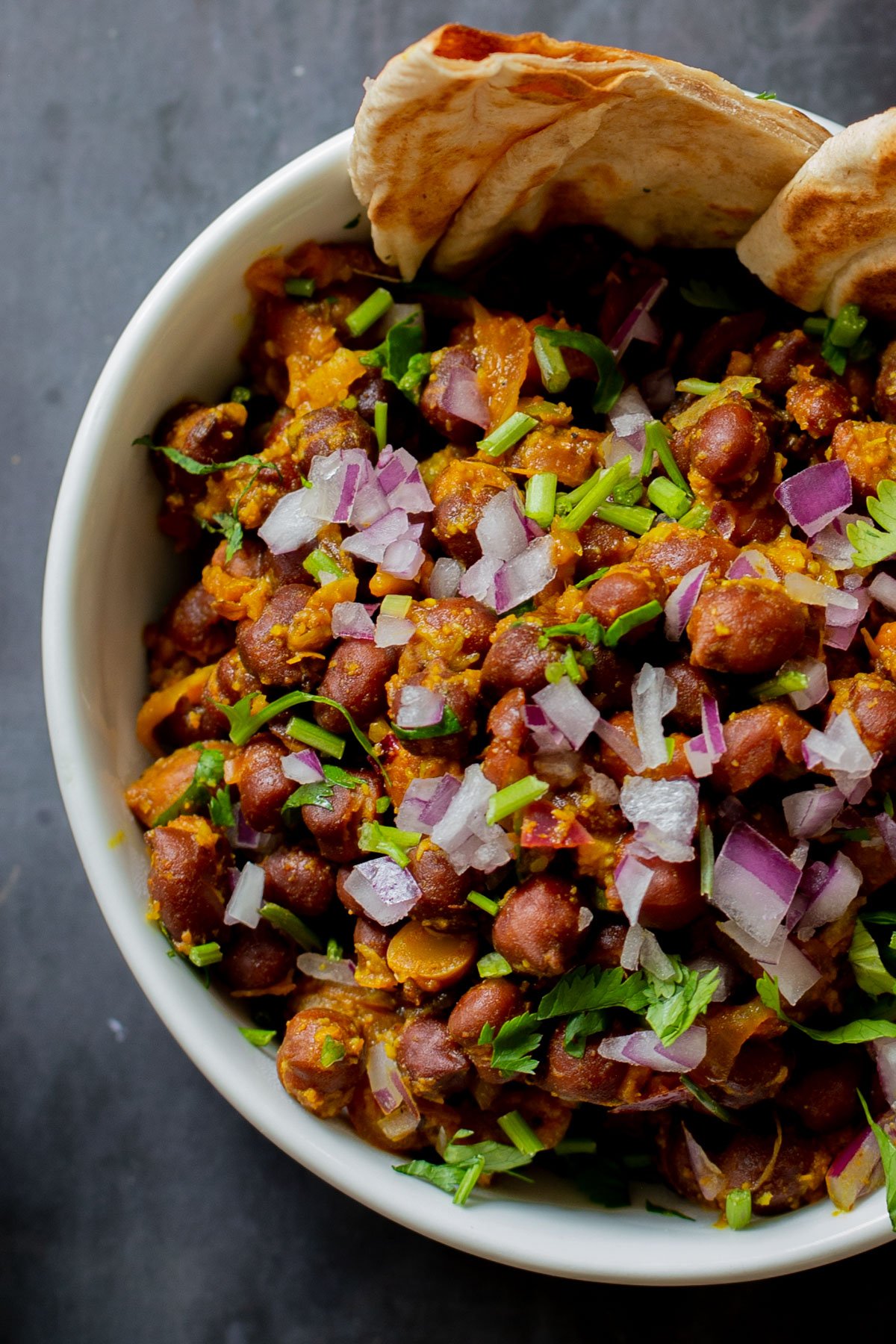 close-up of ghugni garnished with onions, cilantro, and cumin in a bowl