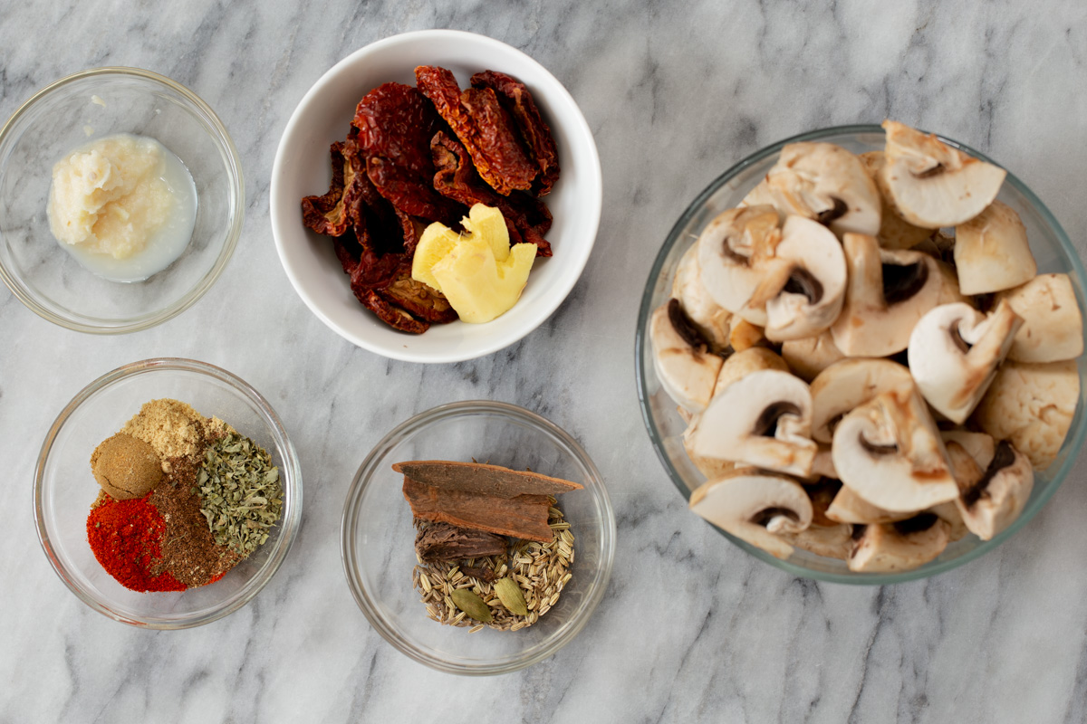 mushrooms, sun-dried tomatoes, and seasonings in bowls on a marble tabletop