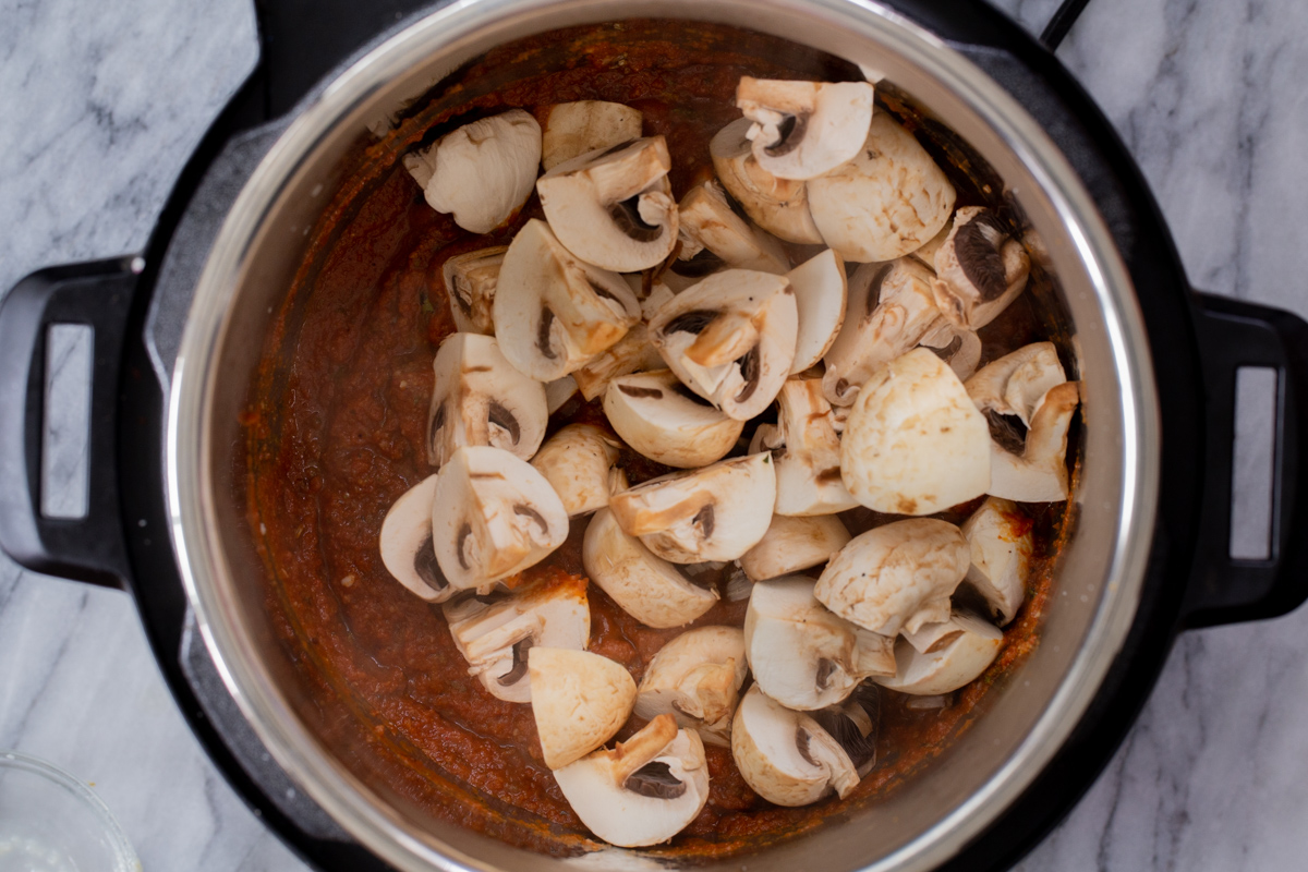 adding mushrooms to the Instant Pot with the sun-dried tomato sauce in it