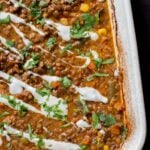 close-up of baked Konkani curry dal topped with coconut cream, cilantro, and pepper flakes in the baking pan