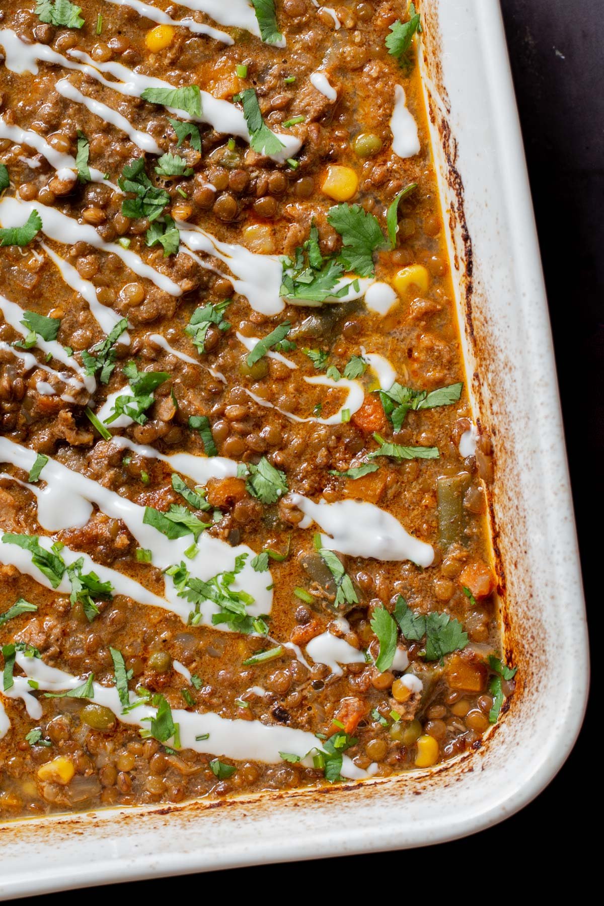 close-up of baked Konkani curry dal topped with coconut cream, cilantro, and pepper flakes in the baking pan