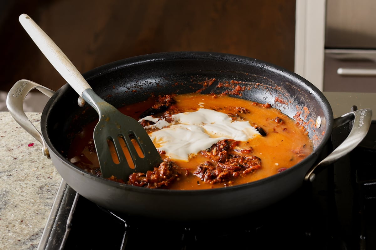 adding water, tomato puree, and yogurt to the pan