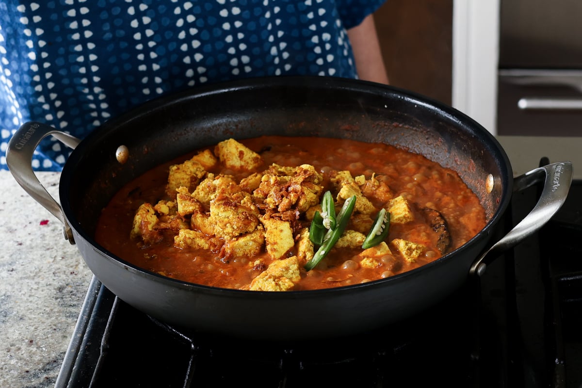 adding green chilis to kosha mangsho sauce in the pan