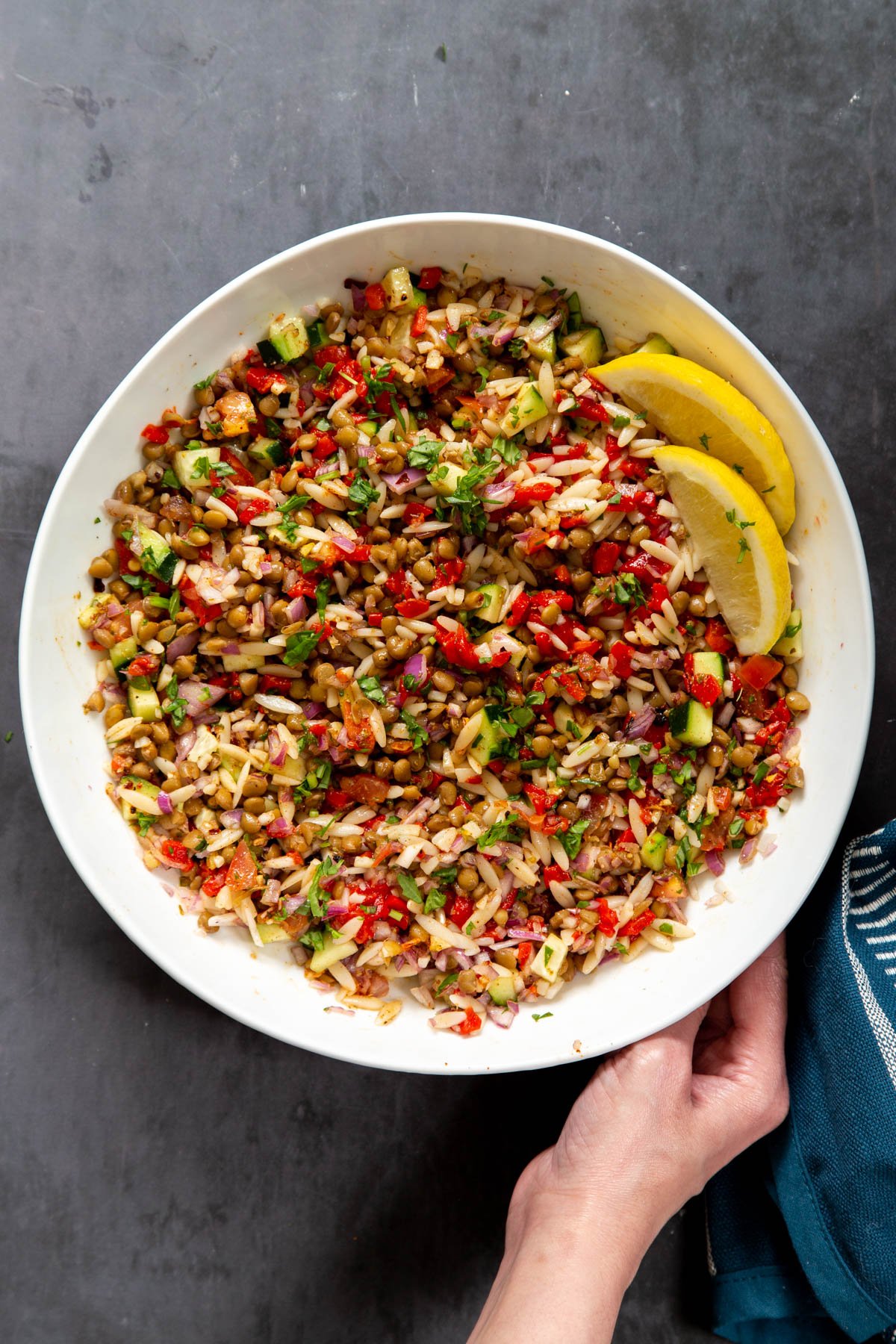 a bowl of lentil orzo salad decorated with lemon wedges 