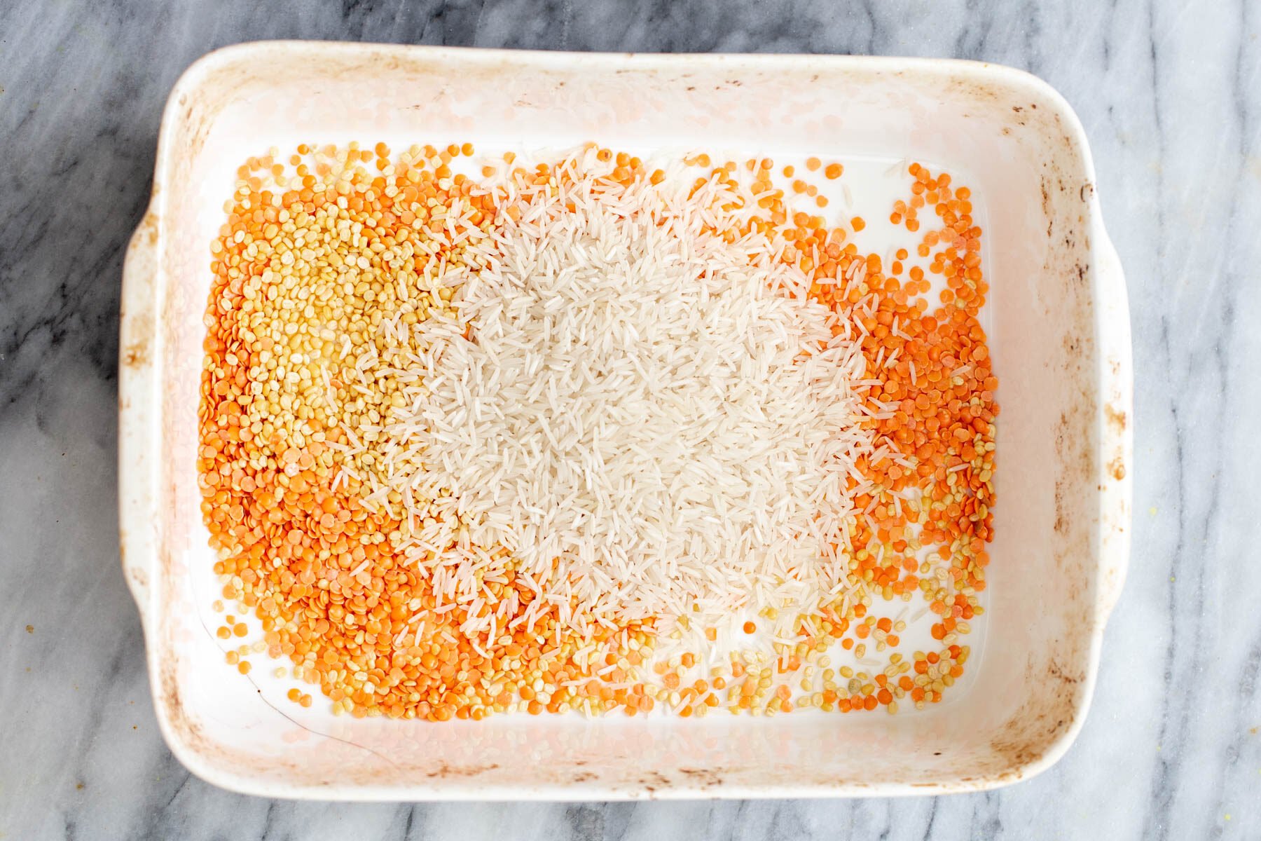 lentils and rice being added to a casserole dish 