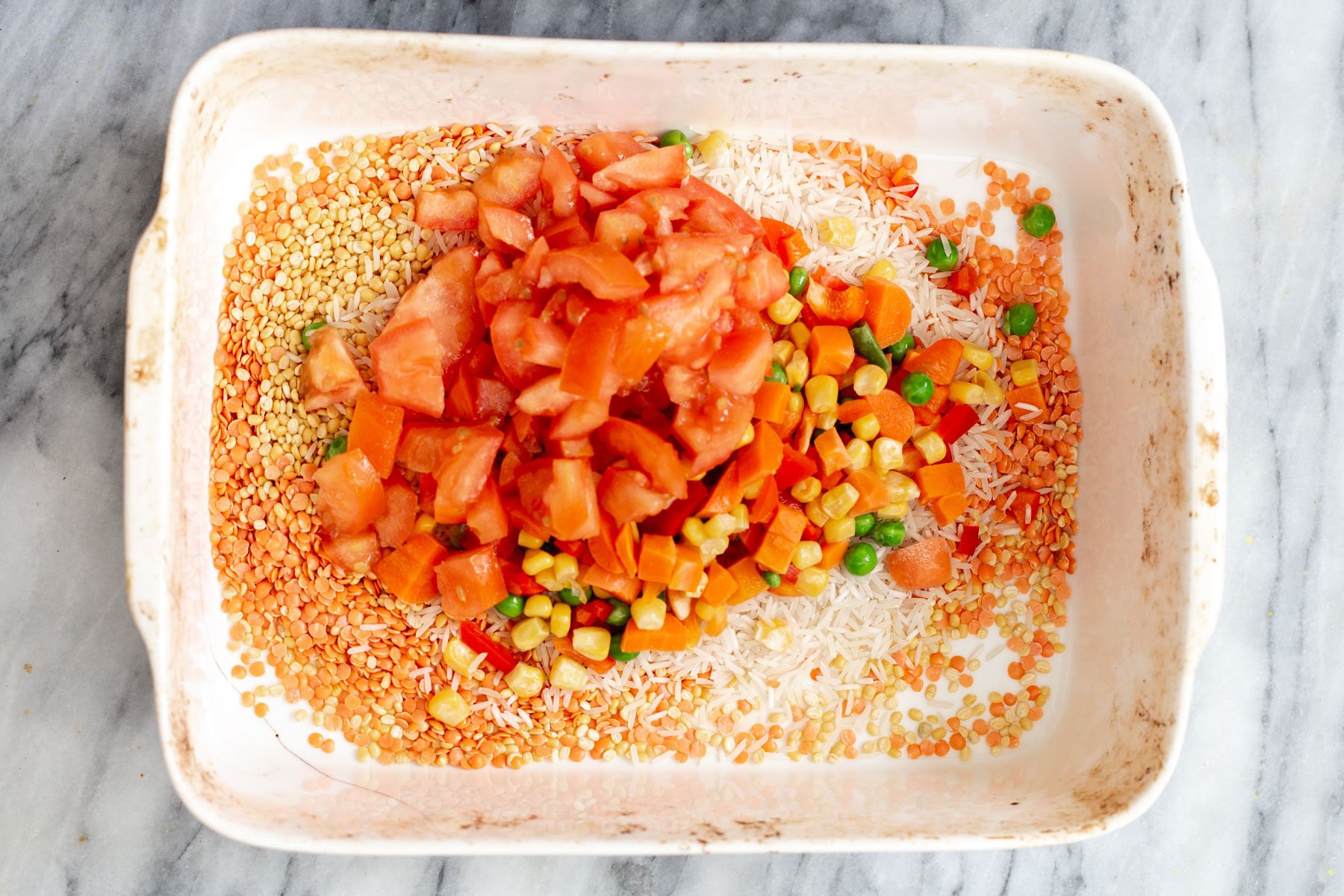 fresh tomatoes and veggies being added to rice and red lentils in a casserole dish