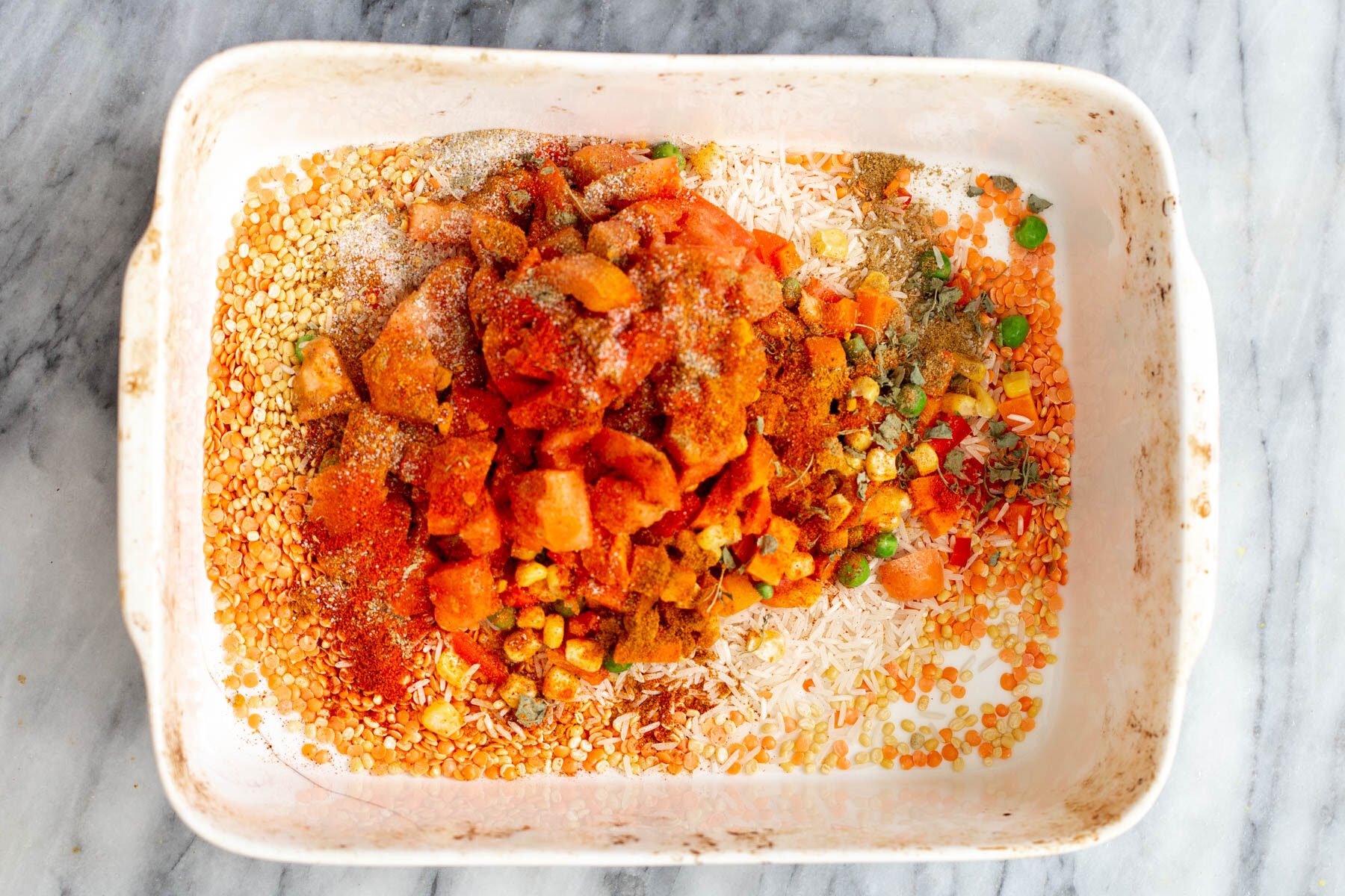 spices being added to rice and lentils in a casserole dish to make kitchari casserole