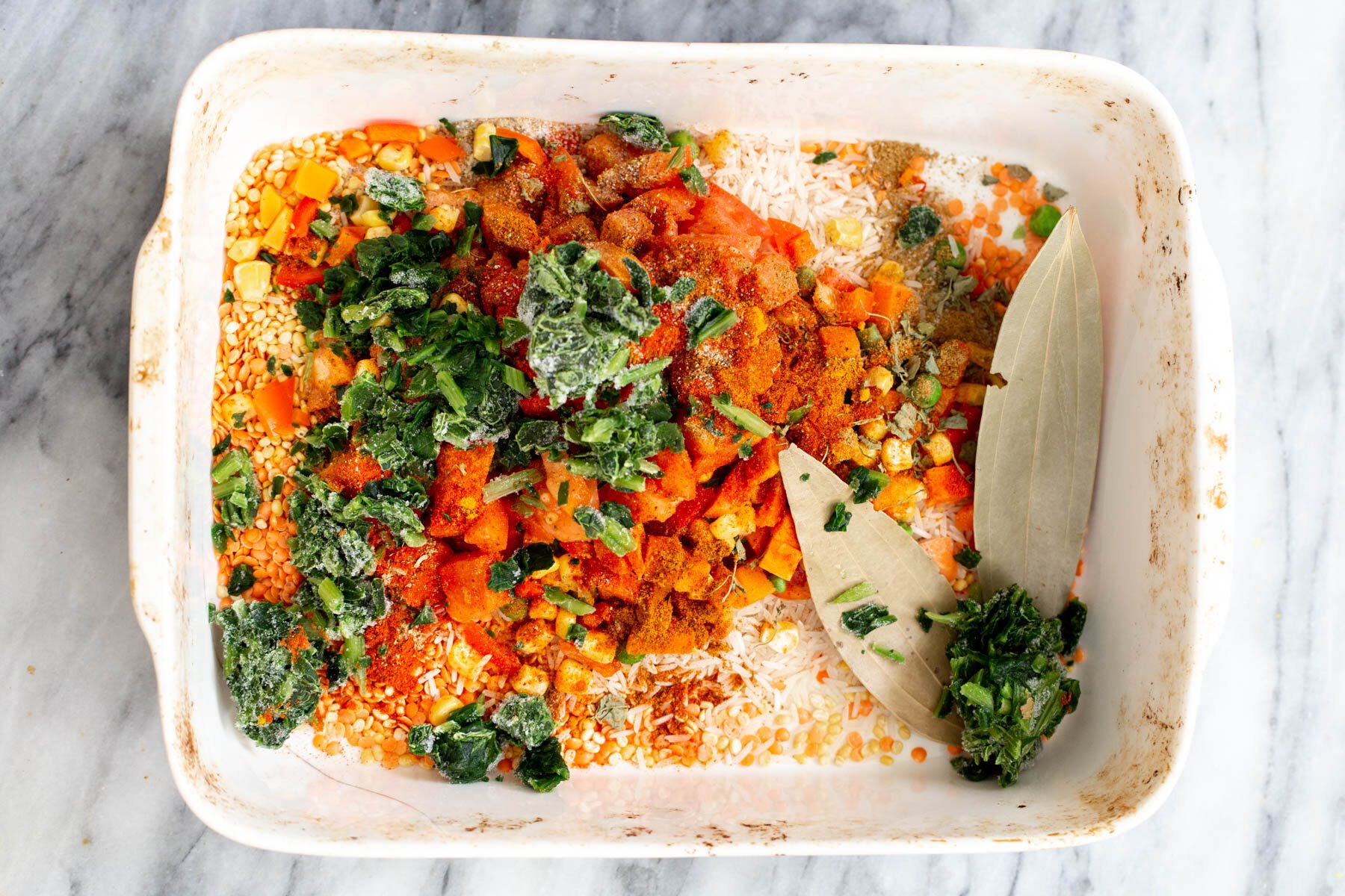 veggies being added to rice and lentils in a casserole dish 