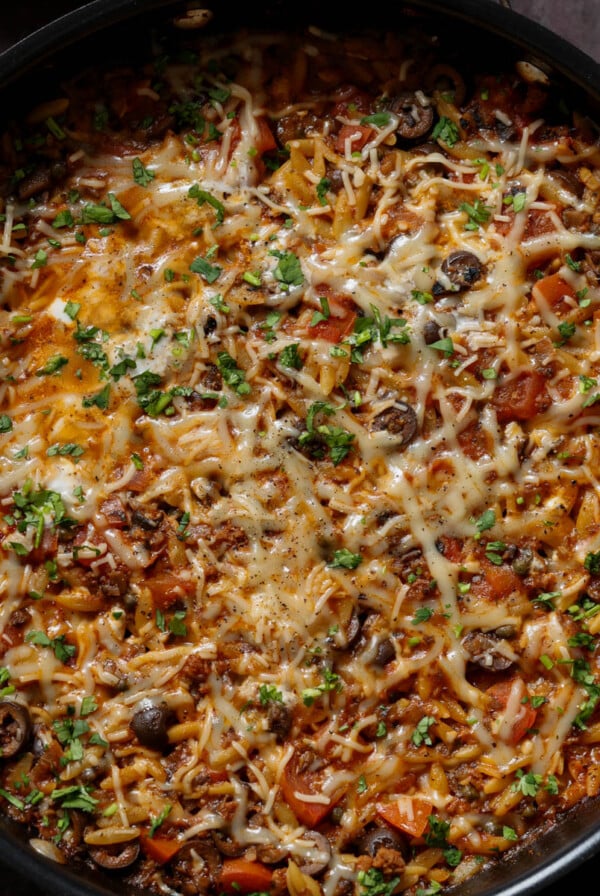 orzo puttanesca in the pan after melting the cheese and topping with herbs and black pepper