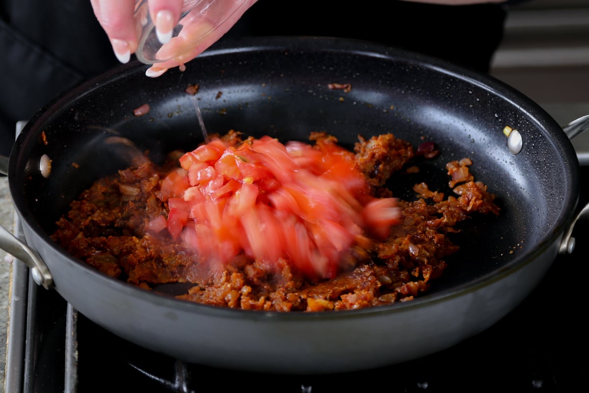 adding tomato to the onions in the pan