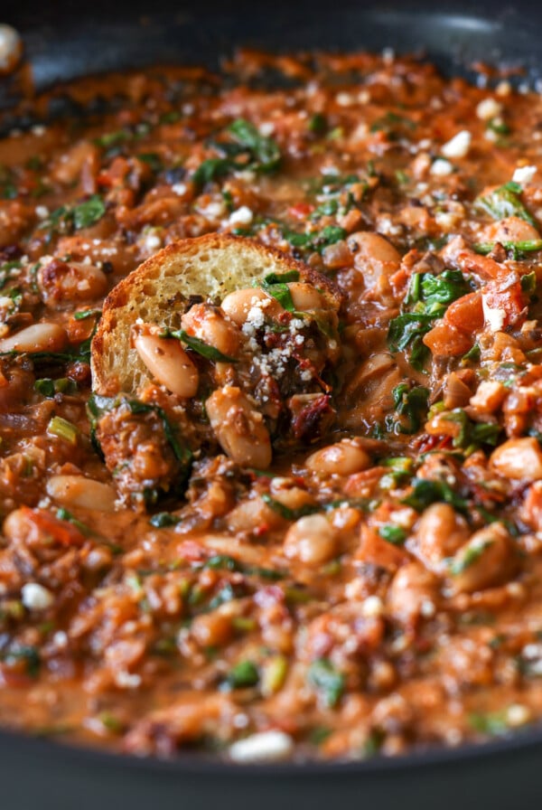 dipping toasted sourdough into vegan sausage pasta sauce in the pan