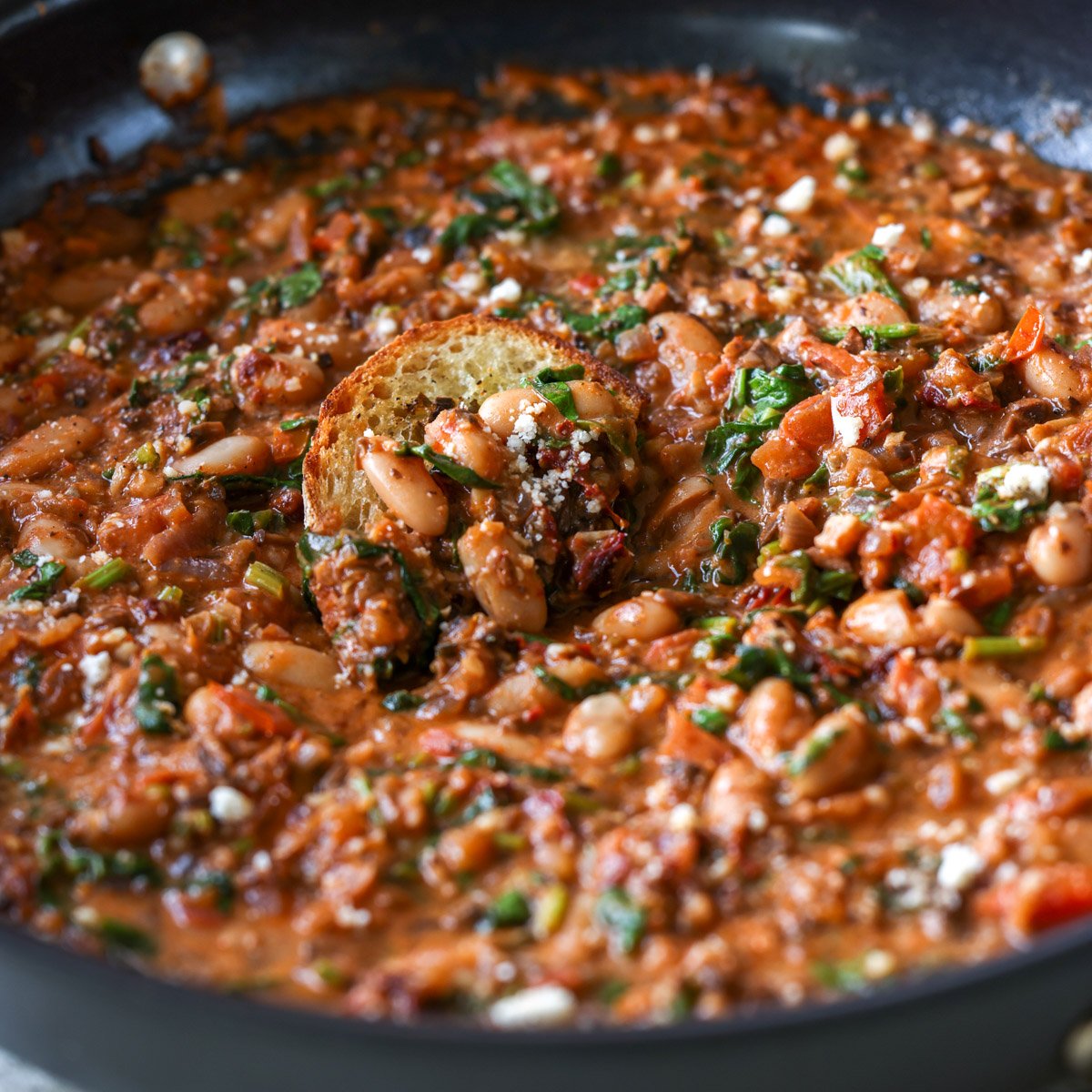 dipping toasted sourdough into vegan sausage pasta sauce in the pan