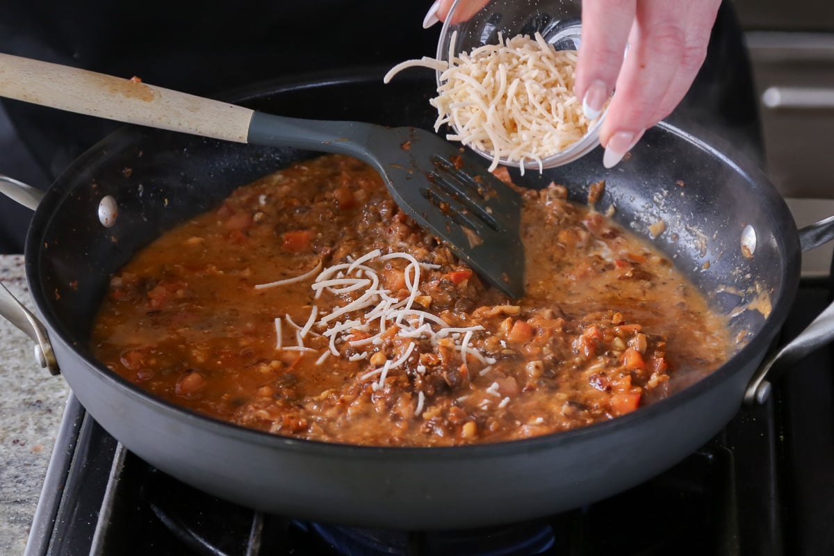 adding vegan parmesan to the pan of vegan sausage pasta sauce