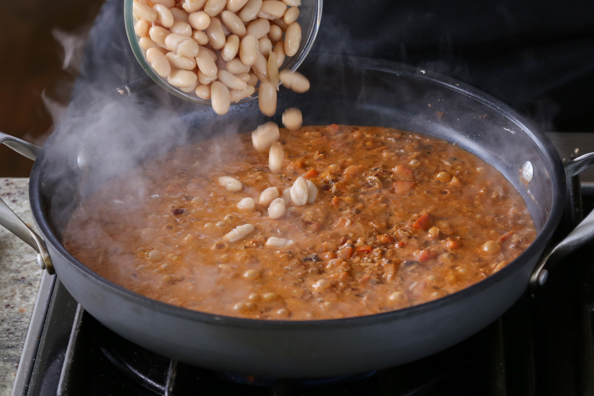 adding beans to the pan of vegan sausage pasta sauce