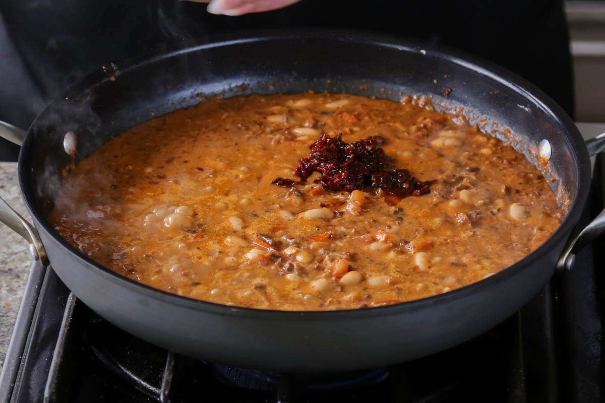 adding sun dried tomato to the pan of vegan sausage pasta sauce