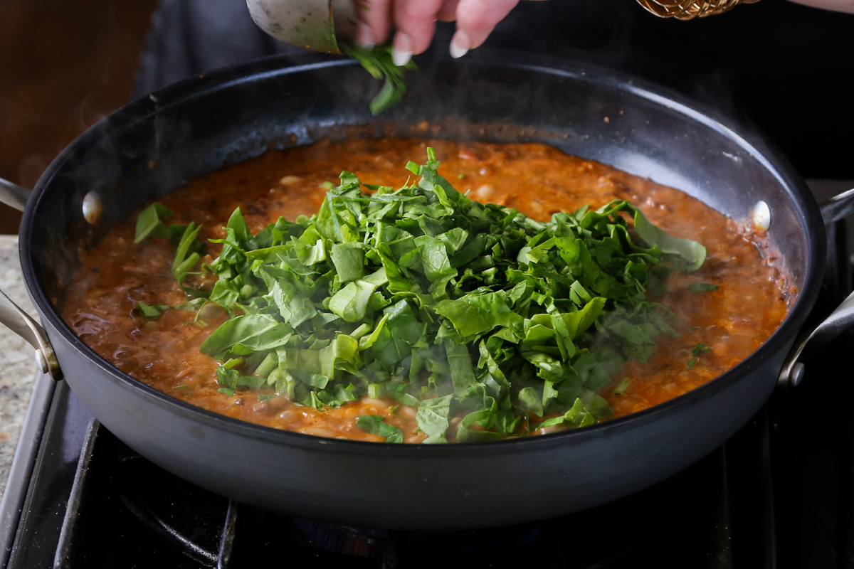 adding spinach to the pan of vegan sausage pasta sauce