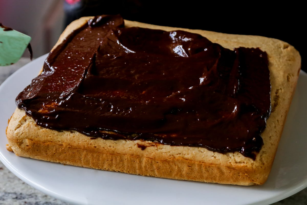 spreading chocolate peanut butter glaze onto the peanut butter cake