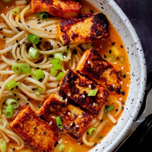 spicy peanut butter ramen in the bowl, after adding tofu, green onions , and sesame seeds