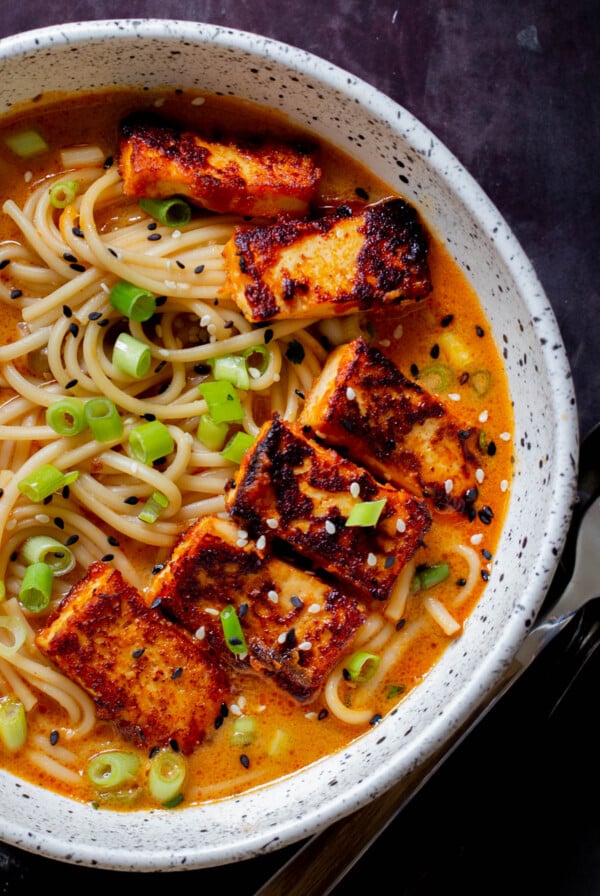 spicy peanut butter ramen in the bowl, after adding tofu, green onions , and sesame seeds