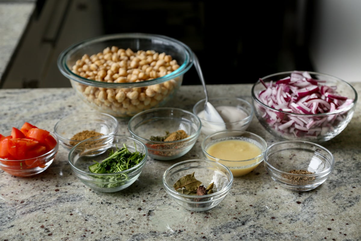 chickpeas, spices, and other chole ingredients in bowls on the kitchen counter