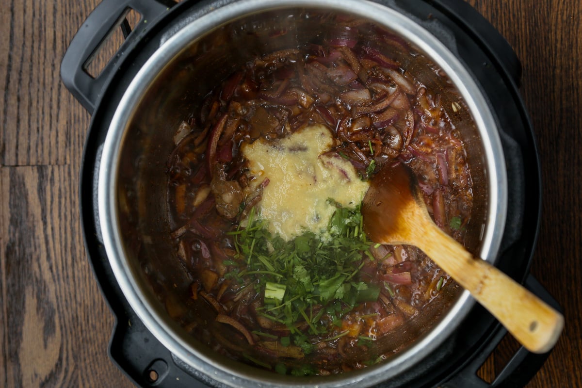 adding ginger garlic paste and cilantro stems to the cooked onions